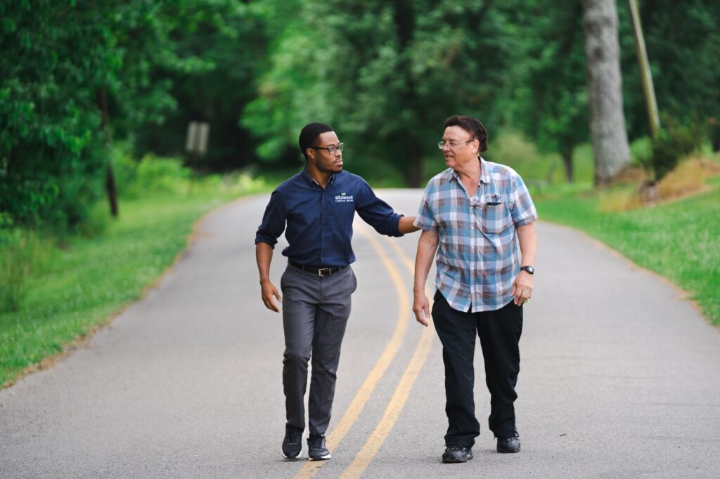 A Wildwood team member walking and talking with a guest on a tree-lined campus road