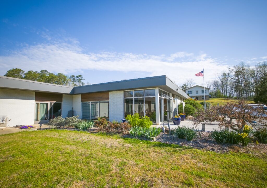 Wildwood’s main campus building, garden beds, and flagpole beneath a blue sky